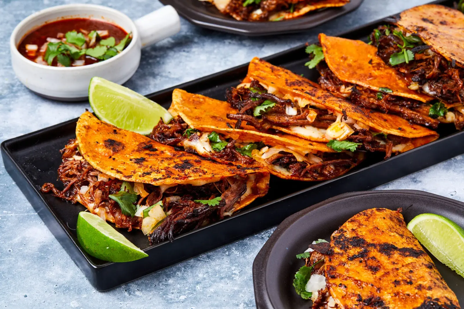Birria taco platter with consommé and lime wedges