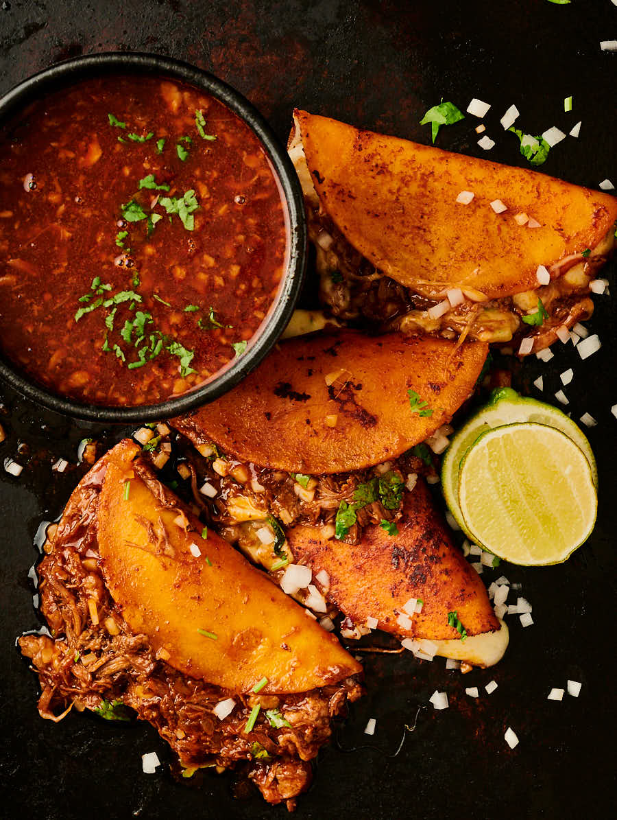 Top-down rustic birria taco spread with consommé