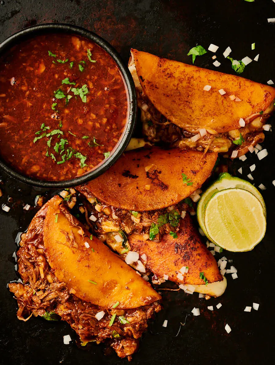 Top-down rustic birria taco spread with consommé