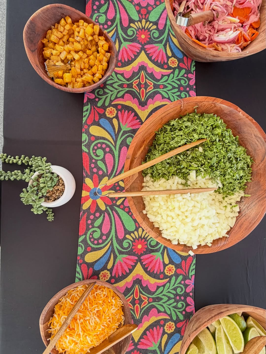 Colorful TacoNTodo garnish bar with fresh toppings on a Mexican textile
