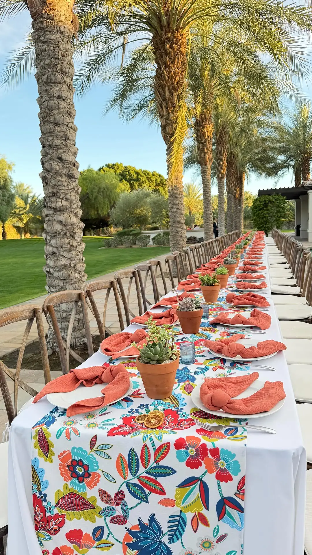 Long wedding rehearsal dinner table with a floral runner under palm trees